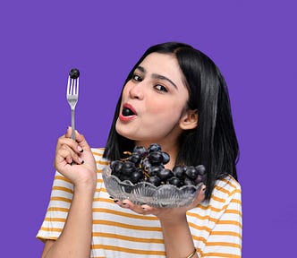 Happy, healthy young woman enjoying a bowl of fresh black grapes
