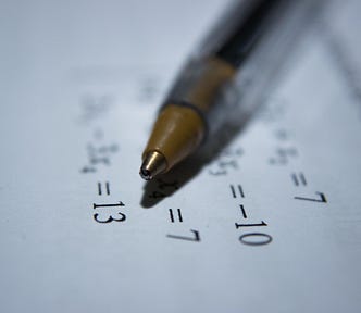 A closeup of a pen lying on a page that has math equations printed on it