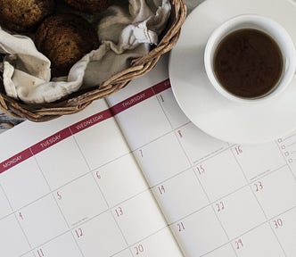 calendar open in month view showing days of the week, along with a cup of coffee and a basket of baked goods.