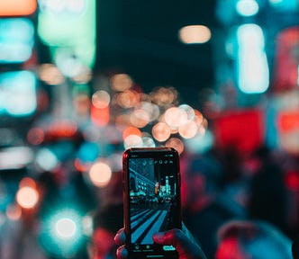 person holding smartphone against bokeh colorful street lights