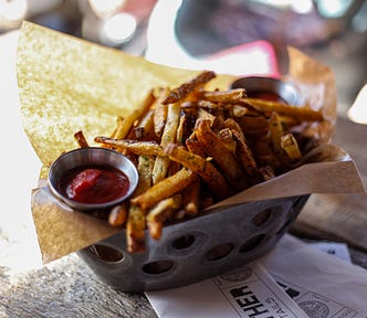 Crispy french fries in a metal basket lined with brown paper and a a small dish of ketchup.