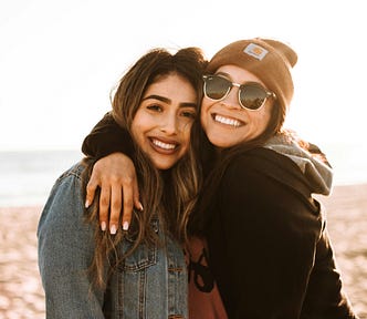 Two women smiling and posing together for a photo at the beach.