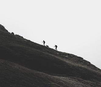 Two people and one dog climbing a steep mountain