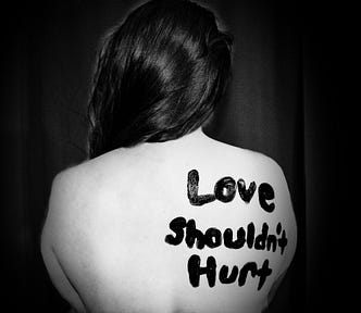 Woman with back to the camera, naked from waist up,the wordsmLove Shouldn’t Hurt written on her back.