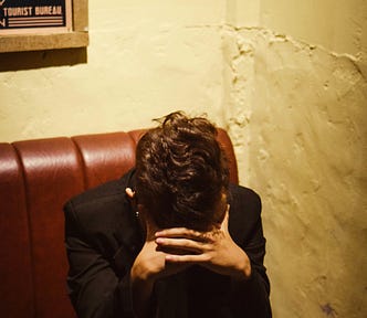 woman sitting in a booth with her head down, appearing to cry