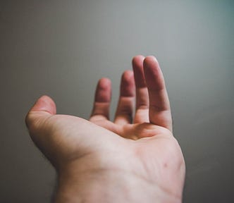 A white hand and wrist stretches out from us. Black background.