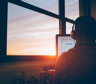 man sitting in front of pc with headphones and sunset analyzing problems