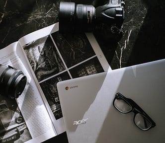 A laptop, camera, book, and a pair of glasses