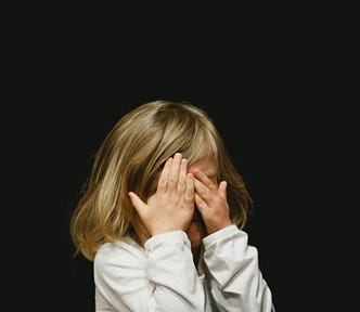 young girl with blonde hair covering her face in despair, black background