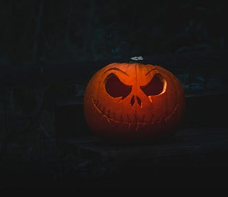 A carved pumpkin face lit from within. It has a wide mocking grin and huge challengign eyes.