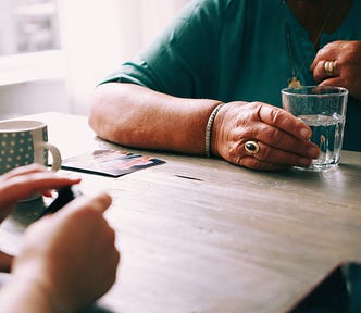 An older hand holding a cup of water across the table from a younger hand