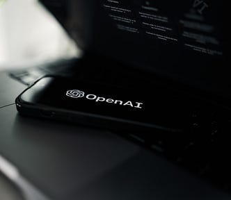 Phone lying on a laptop. Phone has OpenAI logo as the screensaver