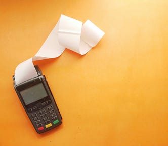 A calculator on a yellow background with a string of paper coming out of it.