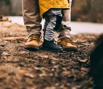 picture of the feet (in boots) of a dad and his son in the dirt