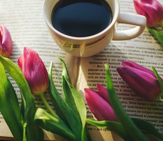 a white cup of black coffee surrounded by beautiful lillat flowers on an open book