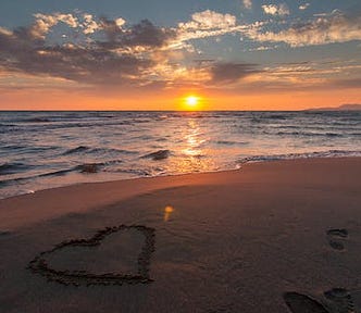 Sunset at beach with heart drawn into sand.