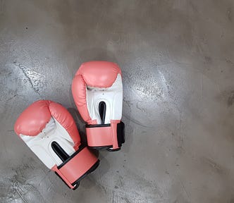A pair of red and white boxing gloves sitting abandoned on a concerete floor