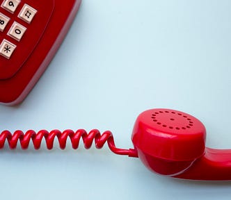 Old red push button phone with cord and handset off the hook