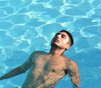 sexy man floating in a swimming pool, eyes closed