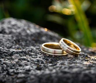Two gold wedding rings, embedded with diamonds, on what appears to be a gray rock.