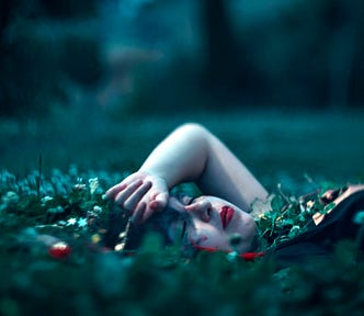 Woman lying in a field of green with her hand lying across her forehead