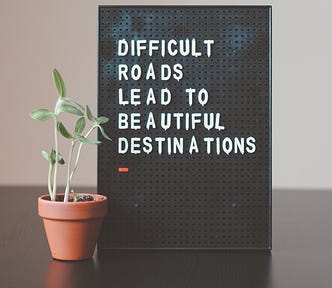 Difficult Roads Lead To Beautiful Destinations written on a board next to a plant.