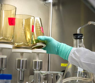 Scientist reaching for beaker of chemicals in laboratory (PFAS, PFOA)