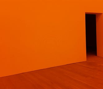 A doorway in a bright orange room, symbolizing the experience of being on the threshold of transition and change.