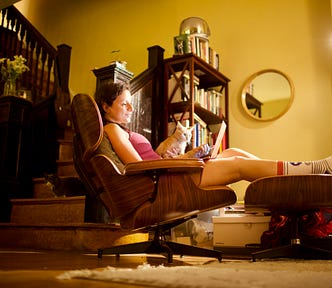 woman sitting with laptop and cat on a chair while resting her feet