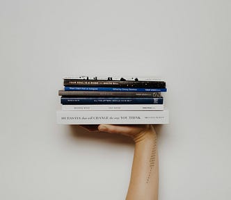 An extended arm, palm flat, supporting a bile of books