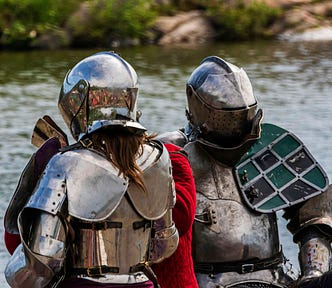 Two people in full plate armour standing by water.