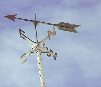 Old weathervane with arrow on top of 4 direction indicators.