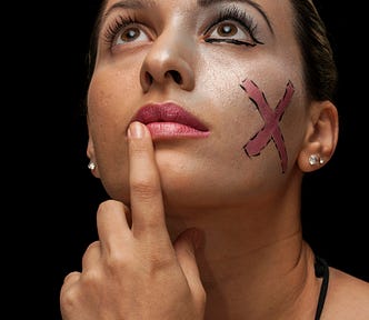 Like what a woman stage actor might look with a black backdrop focusing on her eyes looking up with her pointer finger near her lower closed lips as if questioning, and then half her face is made up with a large red ‘X’ (like a cross-out) on her madeup side as if questioning as to what foods would prevent her from getting acne on her face?