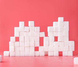 Dozens of sugar cubes are stacked up. Pink background.