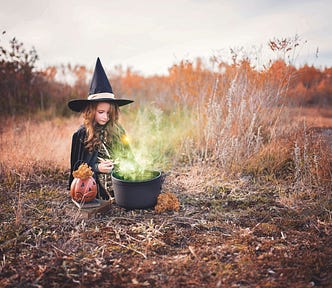 Smol child dressed as a witch and stirring a potion in a cauldron, because why not?