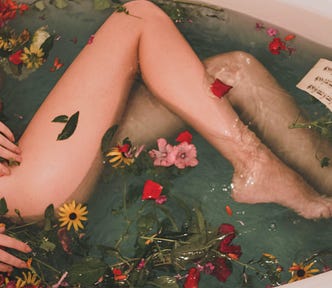 A photo of a bathtub with flowers in it and a partially dressed young woman