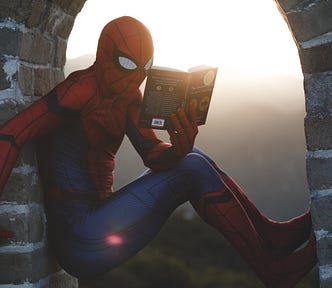 Picture of someone dressed up as Spiderman, sitting in a brick archway as he reads a book with apparent interest.