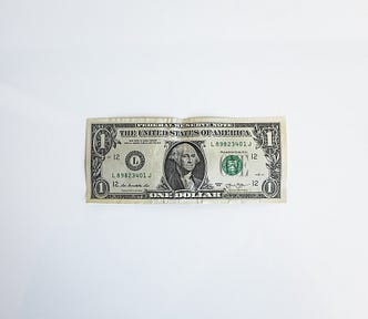 A photo of a US 1-Dollar bill sitting face-up on a flat, white surface.