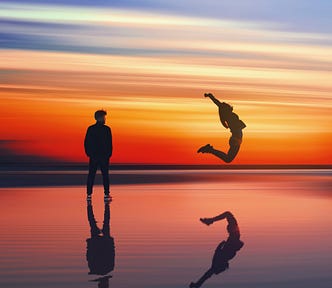 A young woman leaps, her arms and legs flexed behind her, as a man on the left watches. The sun is nearly completely set in the background and the couple appear to be over a thin layer of water. Training in Zone 2 cardio can improve fitness.