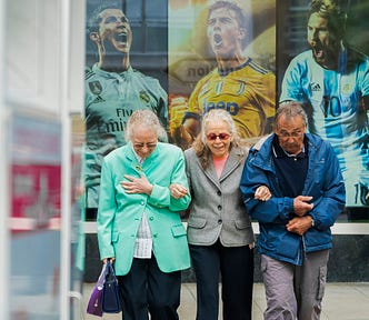 3 elderly people walking in front of a poster of 3 young famous soccer players