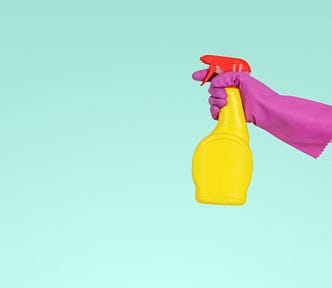 A hand wearing a rubber glove holds a spray bottle.