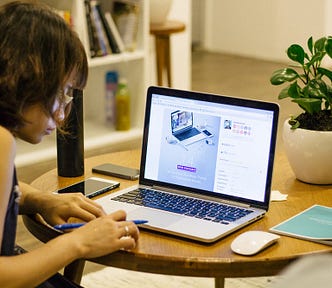 Woman holding pen, using laptop on wooden table with plant.