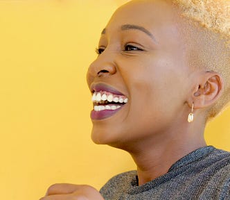 brown skinned woman with a gorgeous smile, head shaved on sides and blond on top