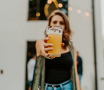 A woman holding a beer toward the camera