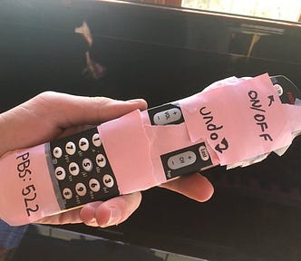 A TV remote with the entire front except the channel and volume buttons covered by pink masking tape.