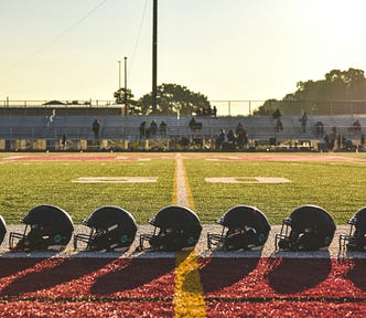 Seven football helmets lined up on the ground next to the 50 yard-line.
