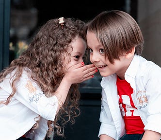 A young girl whispering to a young boy