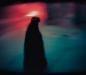 Dark image of a person walking in ethereal red and blue hues.