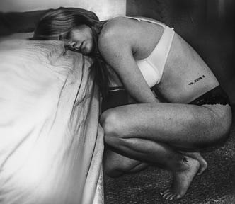 Young woman with face pressed against bed in her underwear.