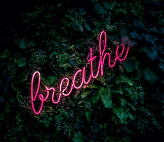 Photo of neon sign saying “breathe” in hot pink against a black background.